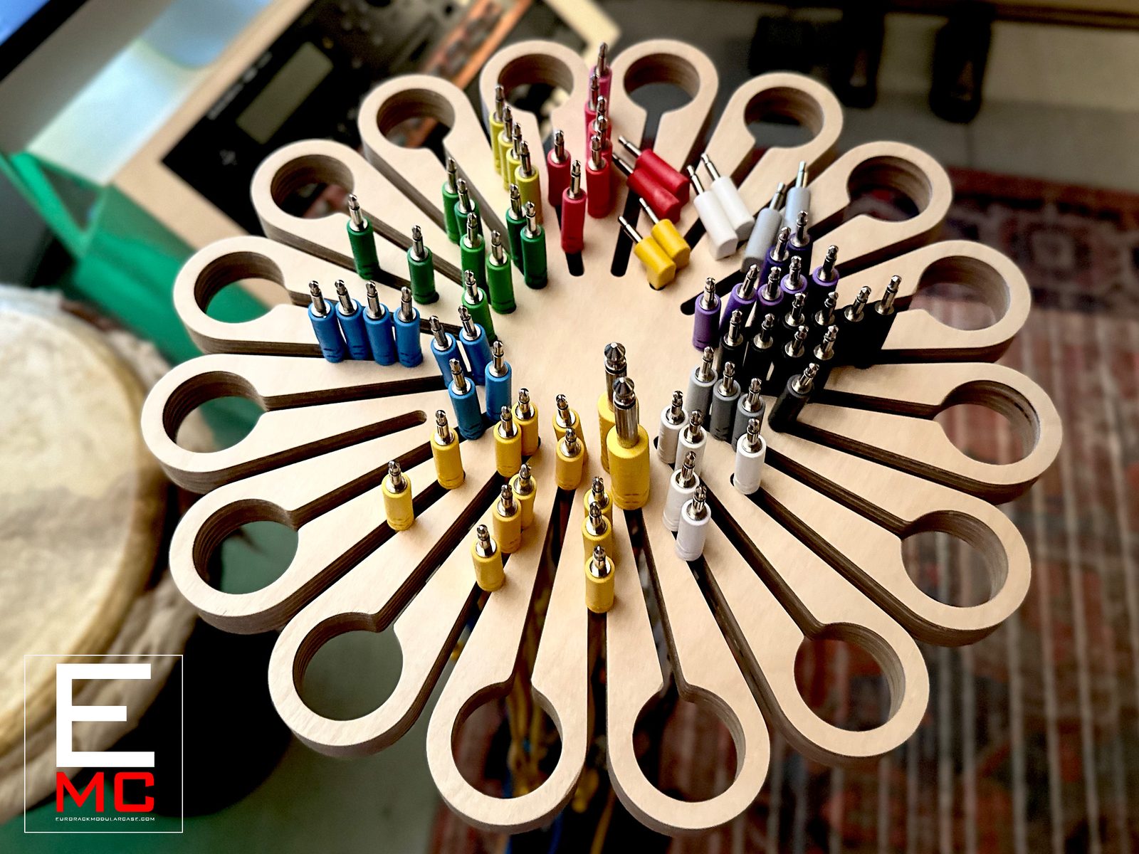 MM304 cable hanger mounted on a mic stand, fully loaded with color-coded patch cables radiating from a 24-arm plywood flower shape, studio desk in background | EurorackModularCase