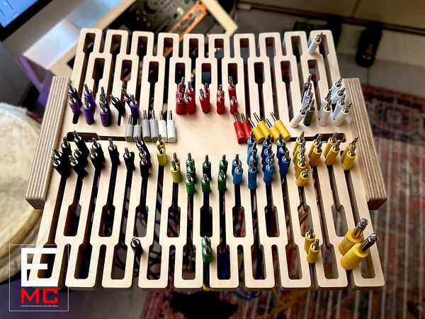 MM434 cable hanger mounted on a mic stand, loaded with color-coded patch cables across its rectangular comb-tooth plywood grid, studio desk in background | EurorackModularCase