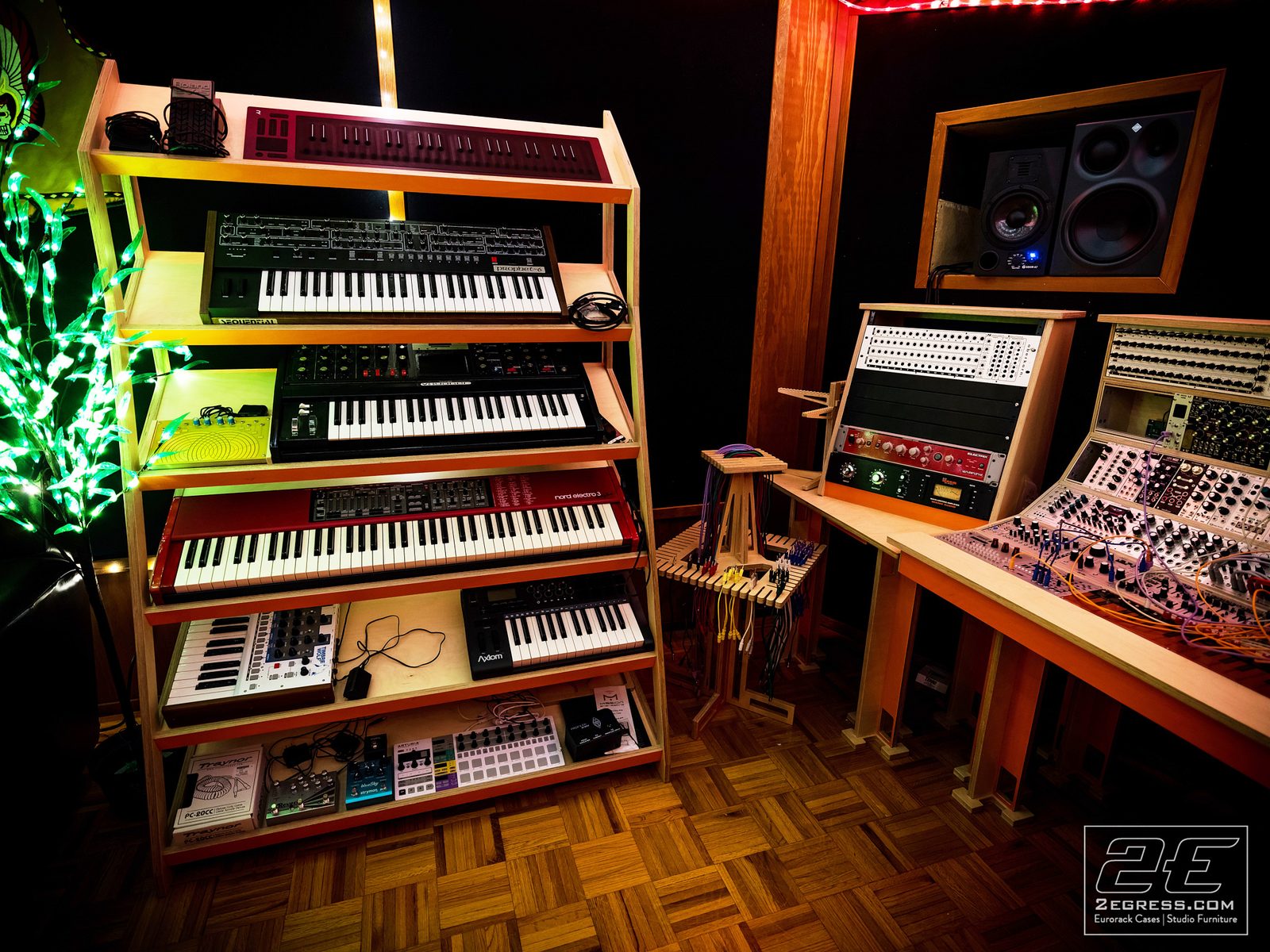 Tyler Doty | Synth shelving unit stacked with keyboards next to a small eurorack patch station | Studio Egregia